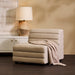 Beige [Brand] chair with textured blanket and elegant lamp.