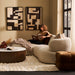 [Brand] beige sofa, woman reading, abstract art, cozy ambiance.