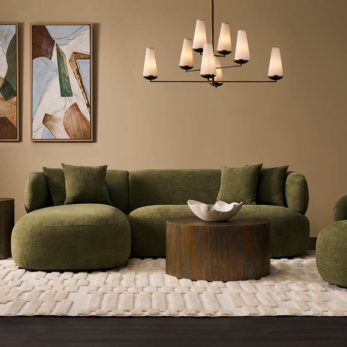 [Brand] green sofa, abstract art, chandelier, wooden table, rug.