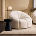 [Brand] plush white armchair with black table and lamp.