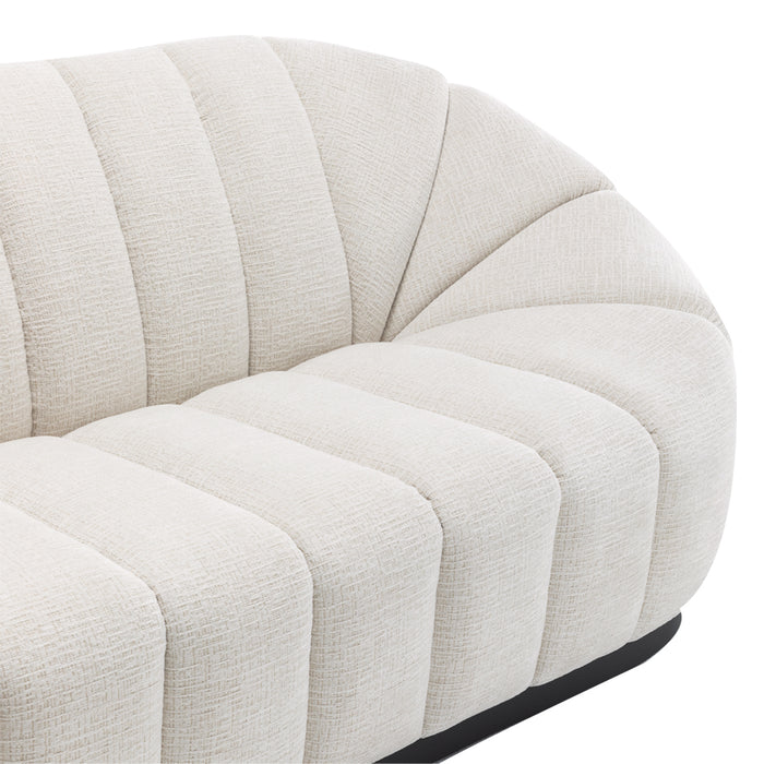 [Brand] cream tufted sofa with curved, modern design lines.