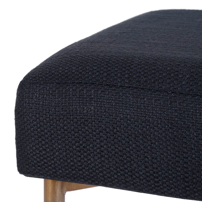 [Brand] black textured ottoman corner with wooden leg detail.