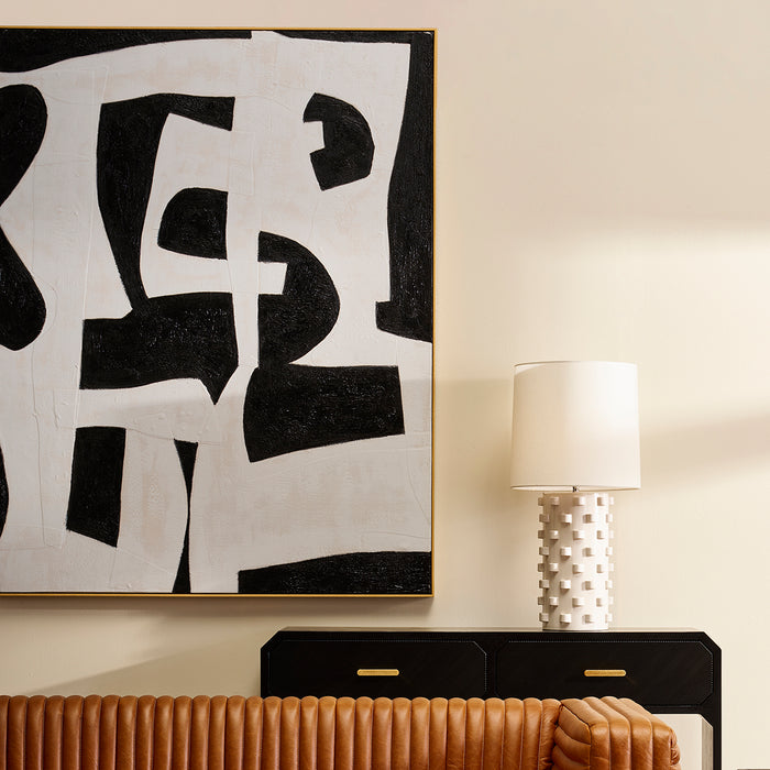 Abstract black and white painting above [Brand] textured lamp.