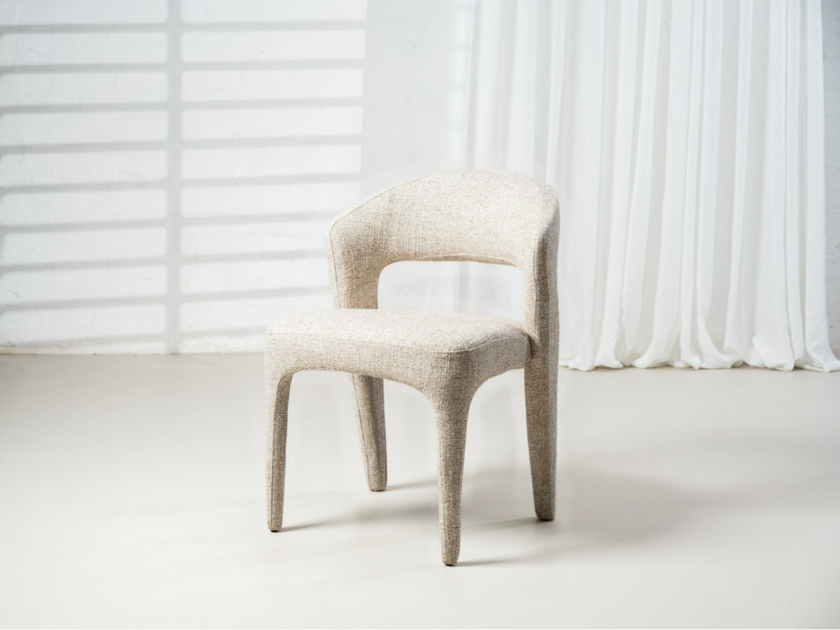 Modern beige chair by [Brand] against white curtain backdrop.